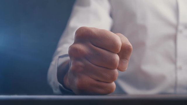 Fist of angry businessman beats on the table in slow motion