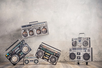 Fototapeta premium Retro old design ghetto blaster boombox stereo radio cassette tape recorders from circa 1980s on handcart front aged concrete wall background conceptual composition. Vintage style filtered photo