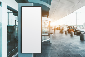 A blank narrow vertical poster mock-up near the entrance of a modern airport terminal with taxis...