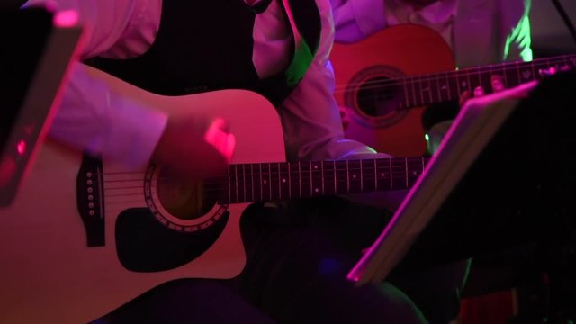 Static Close up shot  of two men dressed in elegant suits playing Acoustic Guitars buy hand. Artists playing on a musical concert in low multi colored light - 1080p, 30fps