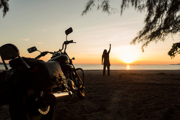 The young man stood on the beach. With a motorcycle parked He raised his hand to the sky. As if he had accomplished something