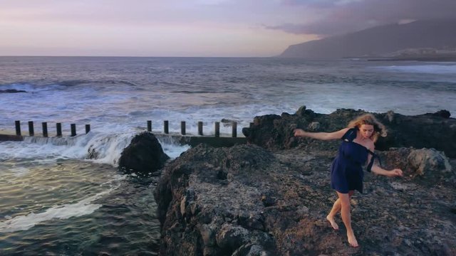 Beautiful, Cheerful and Happy, Blonde Barefoot walks Smiling over the Stones Flying around the Girl with the Movement to Meet for Sunset. Drone shot 4K