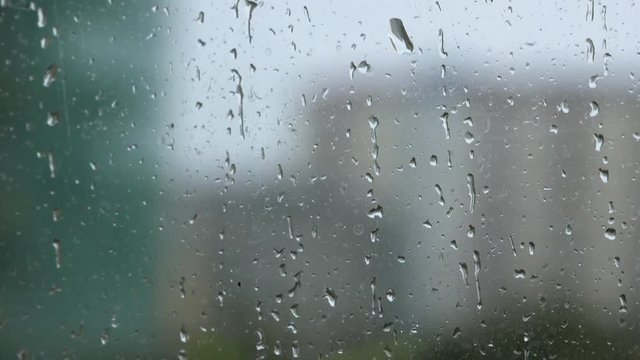 Raindrops on glass window pane during rain shower. Pan up.