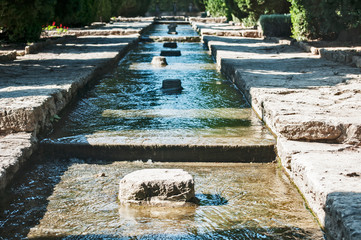 Clear water cascade stream in park garden with stone slabs bed