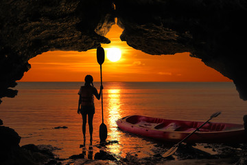 Kayaking in the cave, Asian girls holding the paddle stands in front of a cave by the sea at sunset