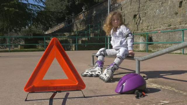 Emergency warning triangle on the road, girl has trouble with rollerblade in park. Conceptual footage in 4K