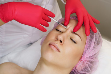 Close-up cosmetologist hands injecting hyaluronic acid between eyebrows to girl. Cosmetic procedure in spa salon. Anti-aging cosmetology