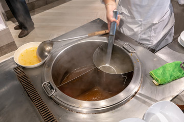 Chef hand boiling noodle with strainer in Thai chamber pot with variety of soup.