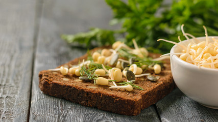 A piece of bread with bran and cereals and sprouted mung beans on a black table.