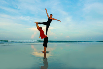 healthy and attractive fit couple of acrobats  doing acroyoga balance and meditation exercise on beautiful desert beach practicing balance and harmony posing