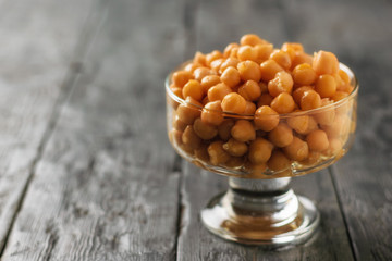 Glass bowl with boiled chickpeas on a dark wooden table.