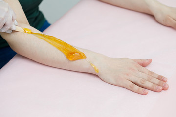 Beautician applying sugaring depilation on arms, hair removal for woman