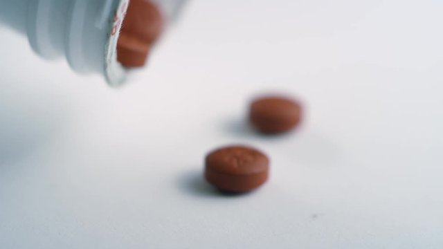 Close-up of brown ibuprofen pills getting poured out of a pill bottle on a white surface