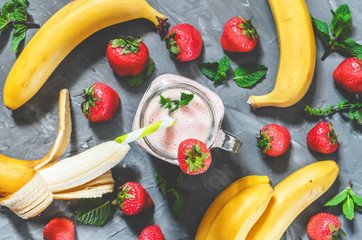 banana and strawberry smoothies with mint in a glass with a straw on the table, top view