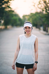 Young woman runner wear white sporty vest, white cap, black short pant do stretching before and after running exercise. Woman runner stretching legs before run during sunny morning on city road.