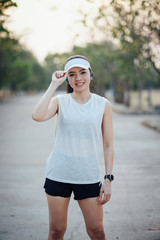 Young woman runner wear white sporty vest, white cap, black short pant do stretching before and after running exercise. Woman runner stretching legs before run during sunny morning on city road.