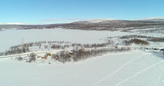 Aerial, drone shot, of a car on route e8, between frozen polar lake and boreal wilderness, in Kasivarren eramaa, Enontekio, Lapland, Finland