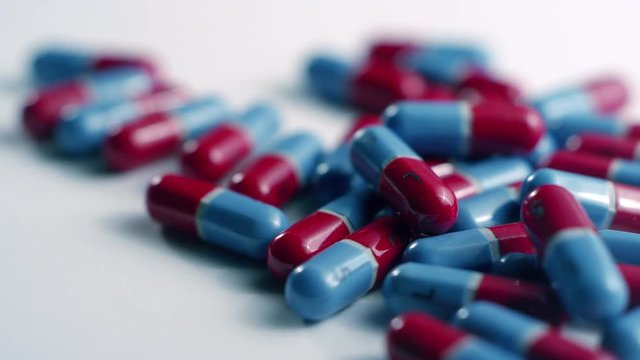 Macro close-up of red and blue acetaminophen capsule pills, spinning left on a white surface