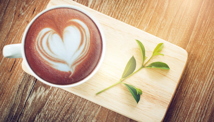 Top view. Closeup coffee in cup with green leaf on wooden table. Vintage color tone