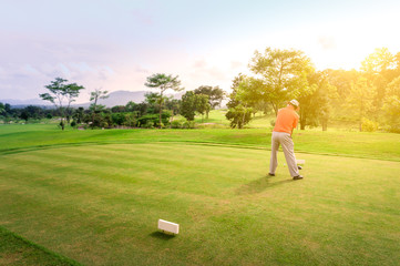 Male golfer teeing off golf ball from tee box on the Course to beautiful sunset