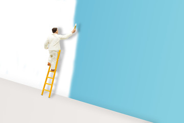 Miniature figurine character as painter standing on wooden ladder and painting wall with paint tools. © Angkana