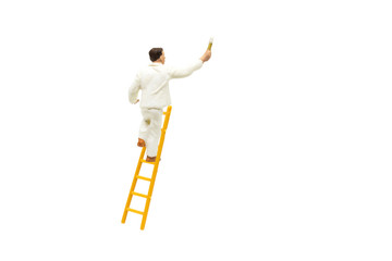 Miniature figurine character as painter standing on wooden ladder and painting wall with paint tools isolated on white background.