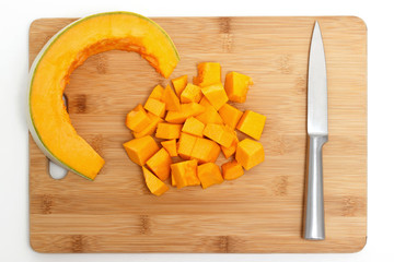 Pumpkin cut into pieces and a knife on a wooden board isolated on white background.