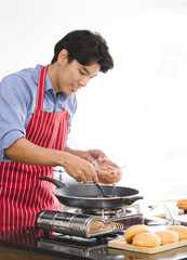 Asian man put ground pork into pan on stove..