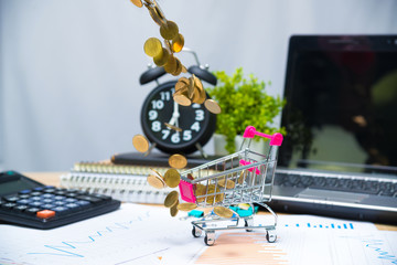 Falling gold coins in shopping cart or supermarket trolley on working table with office supplies or office work essential tools items