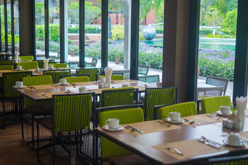 Empty restaurant part of hotel with table and armchair near windows and garden view.