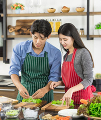  Asian couple in apron make a salad together..