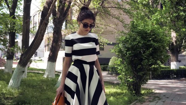 girl in big sunglasses demonstrates combination of black and white striped summer dress and little mustard color handbag