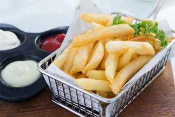 French fries in stainless basket on glass table.