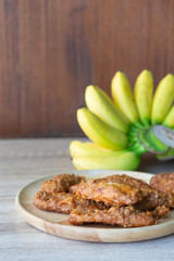Deep fried banana in wooden dish with banana on table.