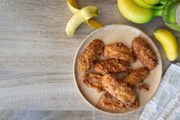 Deep fried banana in wooden dish with banana on table.