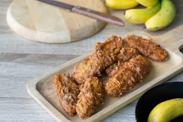 Deep fried banana in wooden dish with banana on table.