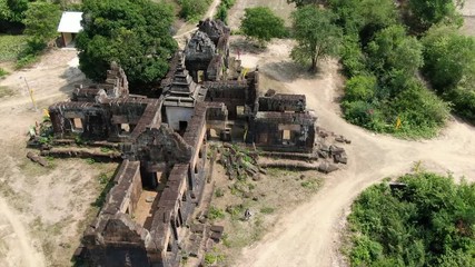 Aerial drone view of ancient Angkor temple complex in Cambodia, Southeast Asia; camera orbits counterclockwise, revealing sun and indistinct traveler below.