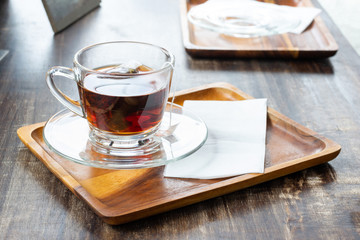 Black tea in glass on wooden tray with tissue on wooden table.