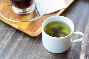 Green tea in teacup and black tea on wooden tray with tissue on wooden table.