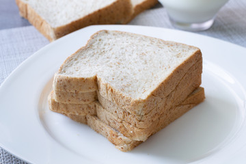Whole Grain Bread in white dish and milk in glass on concrete table.