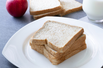 Whole Grain Bread in white dish and milk in glass on concrete table.