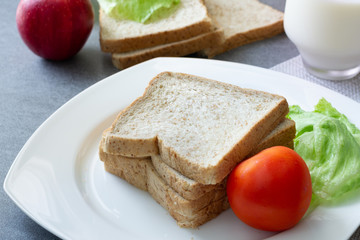 Whole Grain Bread in white dish and milk in glass on concrete table.