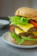Hamburger with beef,cheese,lettuce,onion and tomato in white dish on concrete table.