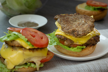Hamburger with beef,cheese,lettuce,onion and tomato in white dish on concrete table.