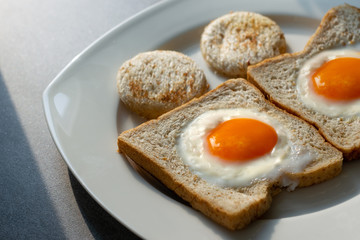 fried eggs in wheat bread in white dish on concrete table with light and shadow in morning.