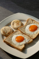 fried eggs in wheat bread in white dish on concrete table with light and shadow in morning.