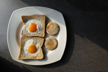 fried eggs in wheat bread in white dish on concrete table with light and shadow in morning.