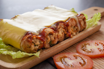 sandwich roll made with wheat bread stuffed chicken and tomato sauce topped up cheese in wooden dish on the concrete table.