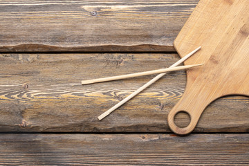 empty cutting board with chopsticks and bunches of brown straw on wooden background, top view 