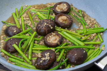 Fried asparagus and shiitake with oyster sauce in pan.